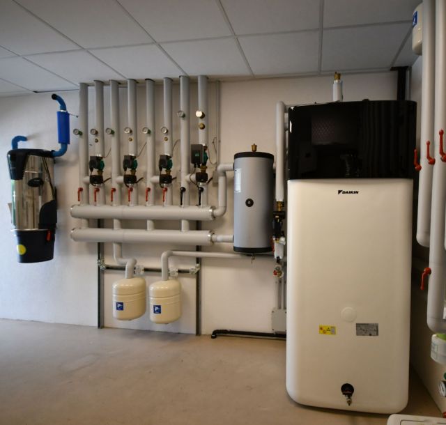 Locale tecnico con impianto idraulico e termico, composto da tubazioni coibentate, pompe di circolazione, valvole, serbatoi e unità per la gestione e distribuzione dei fluidi.